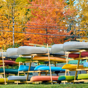A stack of kayaks under trees with brightly colored autumn leaves