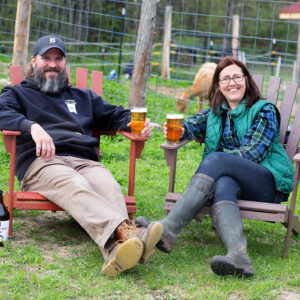 a man and woman holding pint glasses of beer in wooden chairs