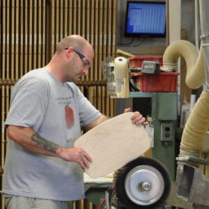 Employee sands wood furniture components at Built By Newport.