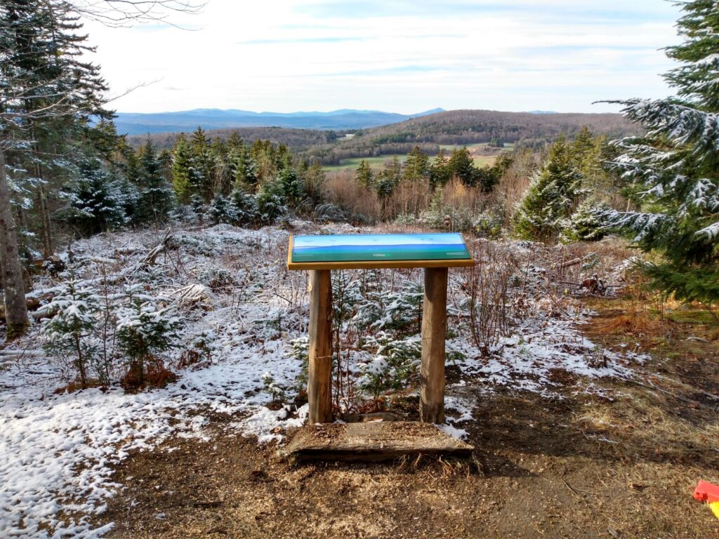 Full color panoramic sign identifies mountains in the view from trail in Greensboro, Vermont.