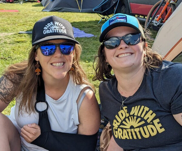 Two women wearing Ride With Gratitude t-shirt and hat.