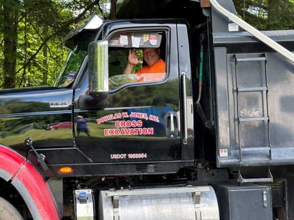 Man from Cross Excavation waves while driving a construction vehicle.