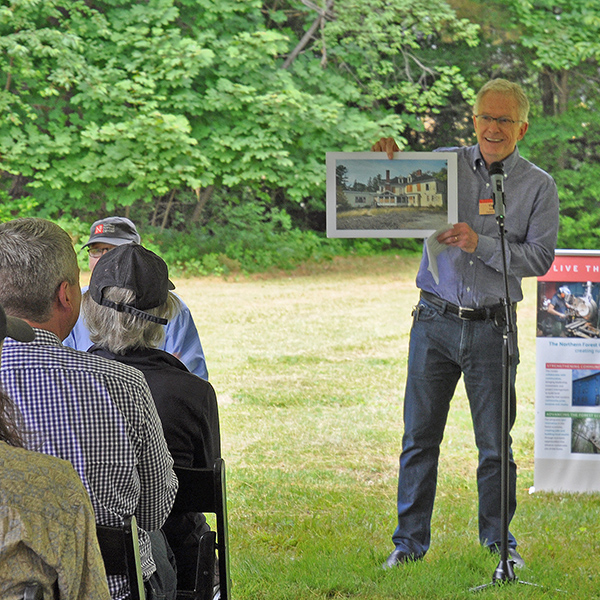 Man displays photo to an audience sitting under a tent