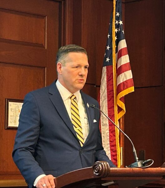 US government official stands at podium in front of US flag.