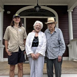 Young man and older couple stand on stairs in front of renovated home.