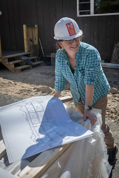 Woman in hard hat looks at construction plans on job site.