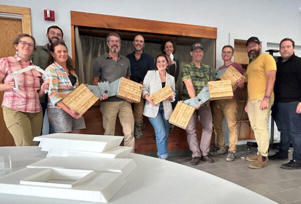 People hold samples of a new system for building with mass timber and proprietary hinges.