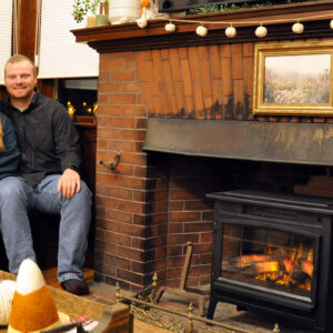 Young couple sits together on bench by wood stove.