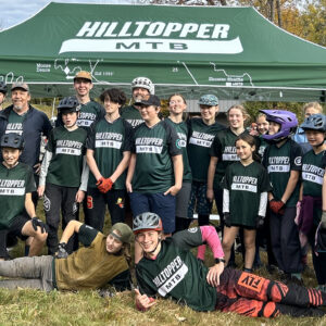 Members of a youth mountain biking program pose for a team photo on a sunny day.