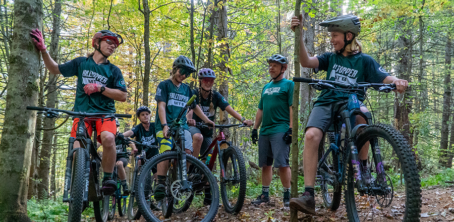 A youth mountain biking group stops to take a break in the woods.